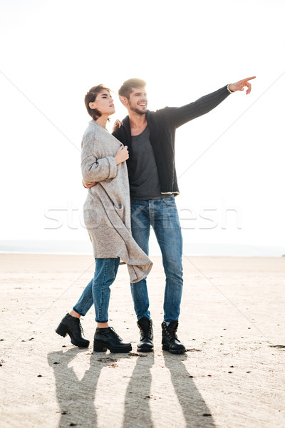 Cheerful young couple standing at the seashore and pointing away Stock photo © deandrobot