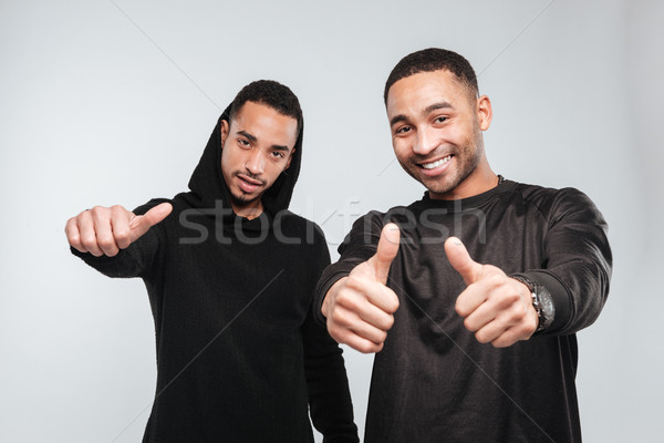 Two cheerful attractive african american young men showing thumbs up Stock photo © deandrobot