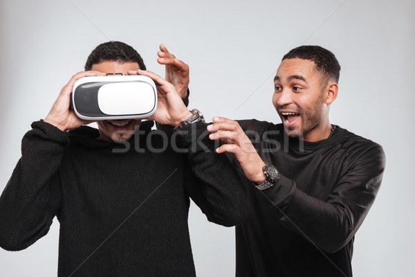 Two attractive smiling african men using 3d virtual reality device. Stock photo © deandrobot