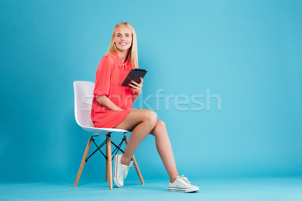 Cheerful smiling woman holding tablet computer and sitting on chair Stock photo © deandrobot