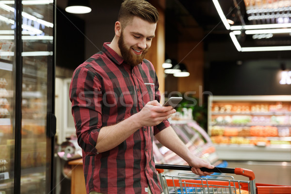 Cheerful young man in supermarket with shopping trolley Stock photo © deandrobot