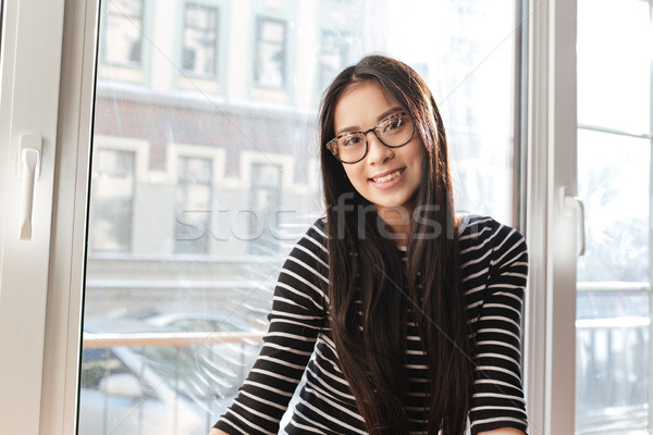Jonge glimlachend asian vrouw vensterbank bril Stockfoto © deandrobot