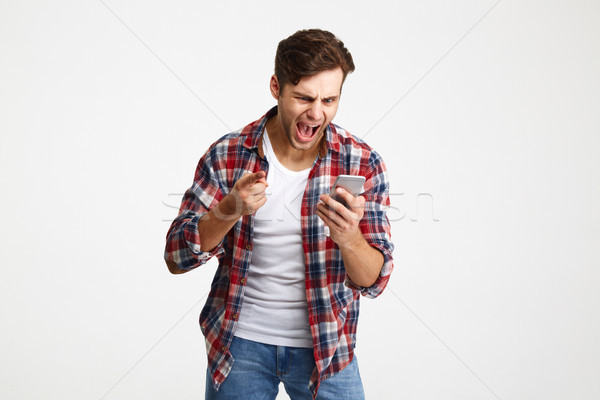 Portrait of an angry unsatisfied man looking at mobile phone Stock photo © deandrobot