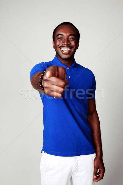 Laughing african man pointing at you on gray background Stock photo © deandrobot