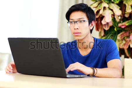Poważny asian człowiek posiedzenia tabeli laptop Zdjęcia stock © deandrobot