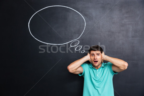 Shocked stressed man covered ears by hands over chalkboard background Stock photo © deandrobot