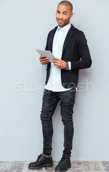 Full length of smiling african american young man using tablet Stock photo © deandrobot
