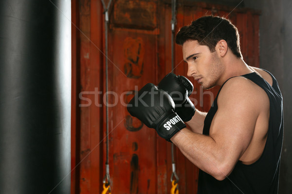 Young strong boxer training in a gym with punchbag Stock photo © deandrobot