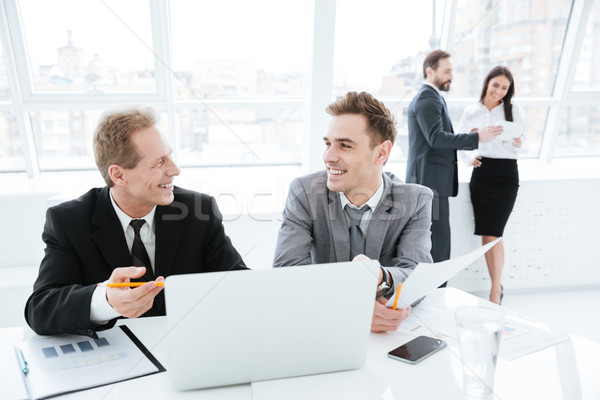 Laughing Business partners by the table with colleagues on background Stock photo © deandrobot