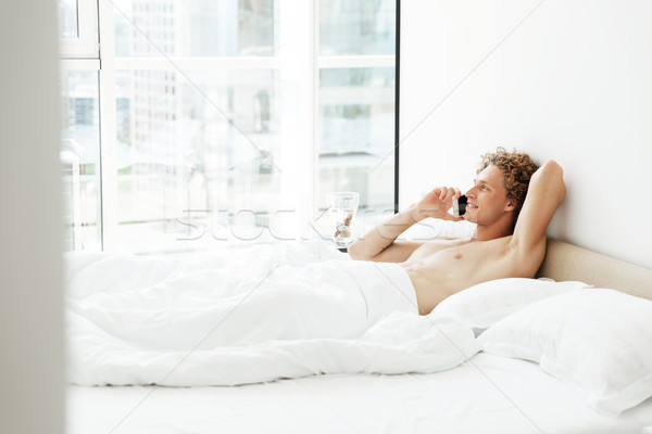 Cheerful man lies in bed at home talking by phone Stock photo © deandrobot
