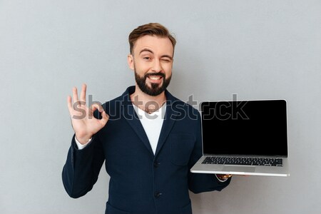 Picture of satisfied bearded man holding silver notebook demonst Stock photo © deandrobot