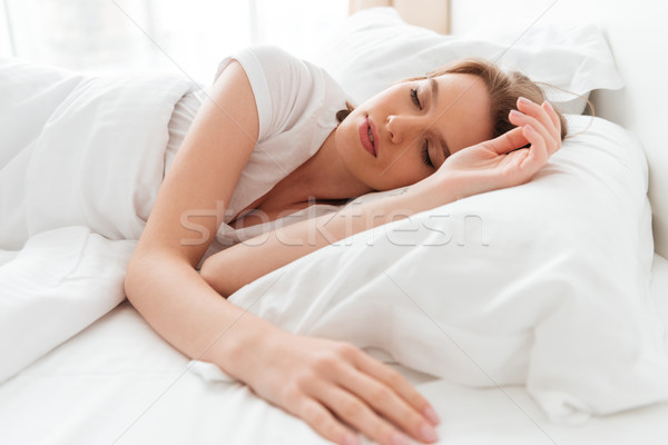 Sleeping young woman lies in bed with eyes closed. Stock photo © deandrobot