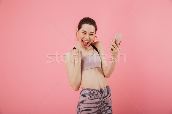 Joyful screaming sportswoman holding smartphone and rejoices Stock photo © deandrobot