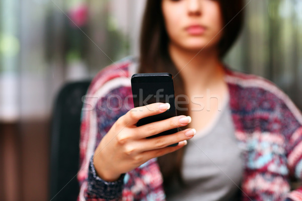 Serious beautiful woman using smartphone at home. Focus on smartphone Stock photo © deandrobot
