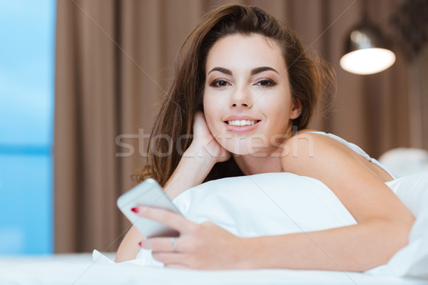 Woman lying on the bed with smartphone Stock photo © deandrobot