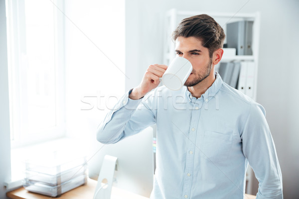 Jóképű fiatalember iszik kávé iroda áll Stock fotó © deandrobot