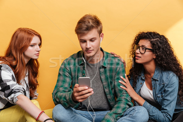 Two women sitting with man listening to music from smartphone Stock photo © deandrobot