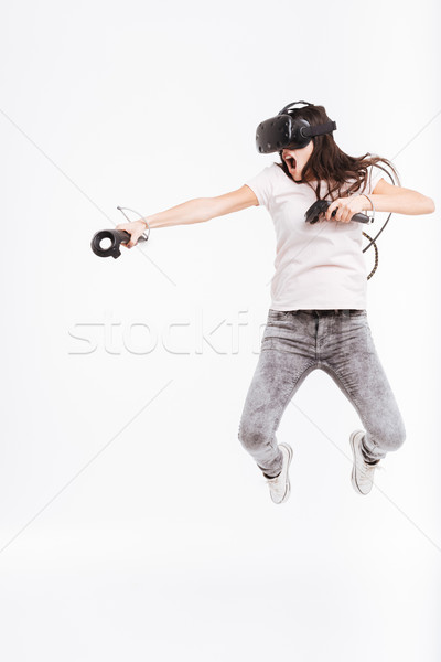 Pretty woman wearing virtual reality device holding joysticks and jumping Stock photo © deandrobot
