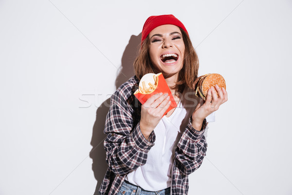 Hungry laughing woman holding fries and burger Stock photo © deandrobot
