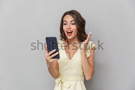 Stock photo: Surprised young woman looking at mobile phone in her hand