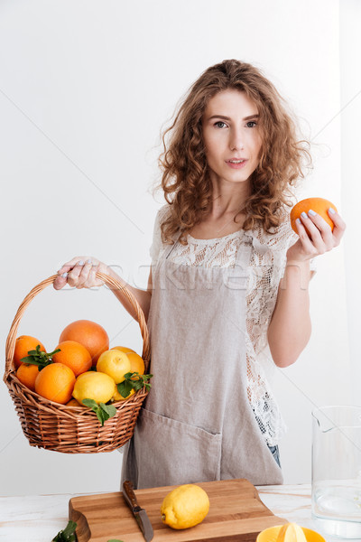 Concentrated young woman holding basket with a lot of citruses Stock photo © deandrobot