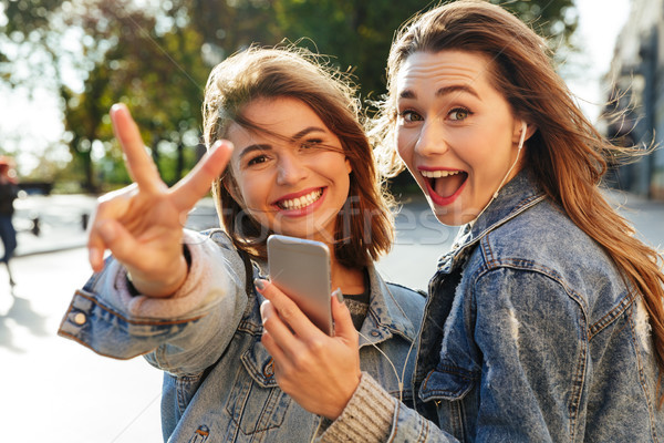 Stock photo: Two happy teen girl showing peace sign while listening to music 