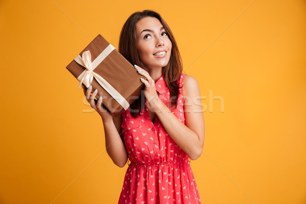 Intrigued runette woman in dress holding gift and looking up Stock photo © deandrobot