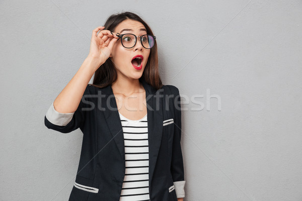 Shocked business woman in eyeglasses looking away with open mouth Stock photo © deandrobot