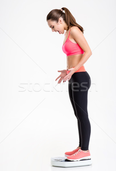 Dazed angry screaming young sportswoman standing on weighing scale Stock photo © deandrobot