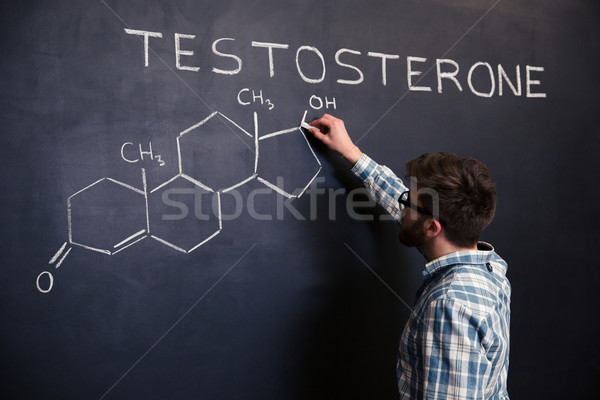 Concentrated student drawing chemical structure of testosterone molecule on blackboard  Stock photo © deandrobot