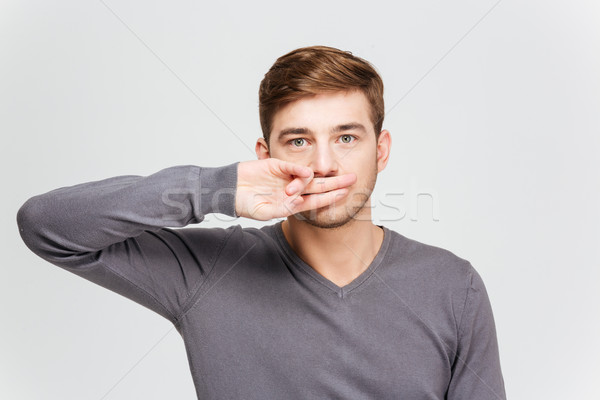 Serious handsome man in grey pullover covered mouth by fingers Stock photo © deandrobot