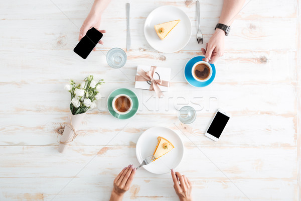 Hands of couple eating cakes and using smartphones on table Stock photo © deandrobot
