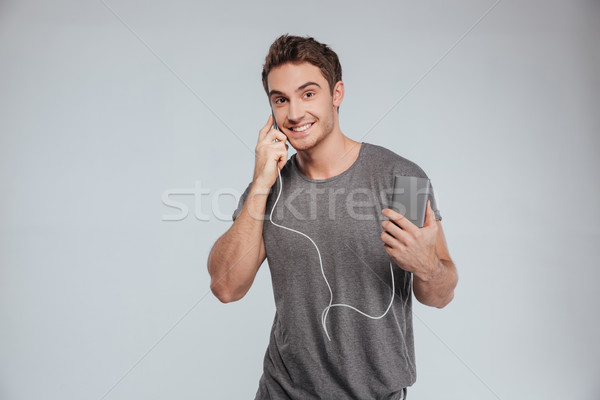 Stock photo: Smiling casual man talking on mobile phone and charging it