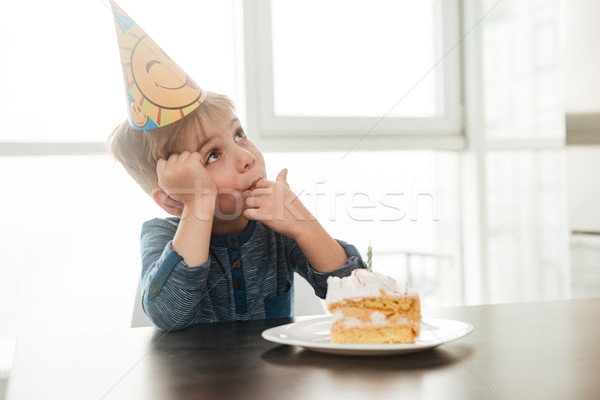 Cute birthday boy sitting in kitchen near cake and eating. Stock photo © deandrobot