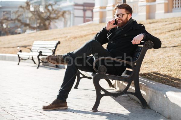 Smiling man in glasses talking on mobile phone on bench Stock photo © deandrobot