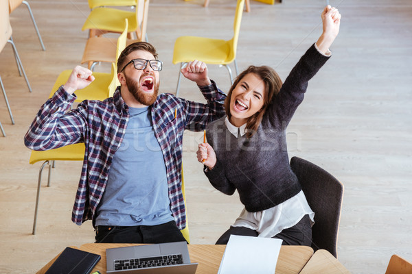 Happy students sitting in library make a winner gesture. Stock photo © deandrobot