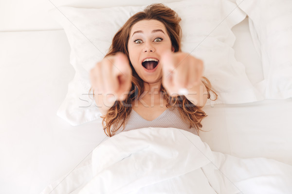 Szczęśliwy młoda kobieta wskazując kamery bed rano Zdjęcia stock © deandrobot