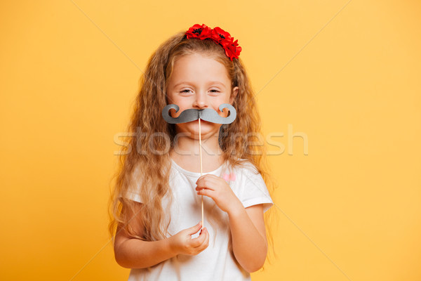 Funny little girl holding fake moustache looking camera. Stock photo © deandrobot