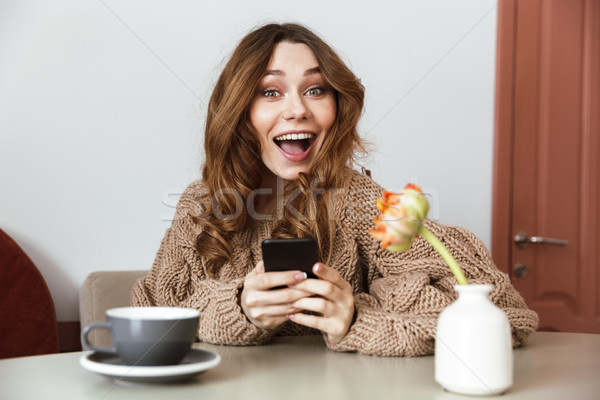 Image of joyful brunette woman holding smartphone in hands, whil Stock photo © deandrobot
