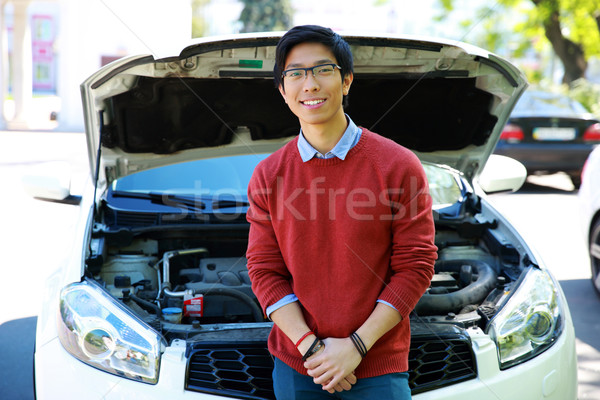 Young asian man standing near car with bonnet open Stock photo © deandrobot