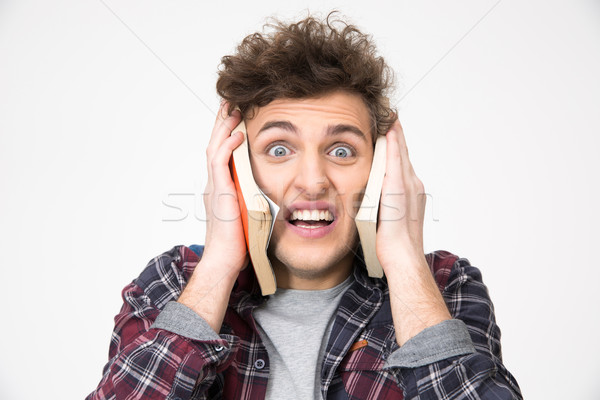 Stock photo: Young male student covering his ears with books over gray background