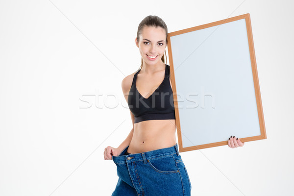 Stock photo: Girl in old jeans became too big holding blank board