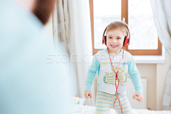 Little boy in headphones listening to music standing on bed Stock photo © deandrobot