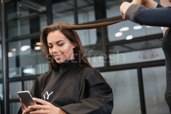 Woman with smartphone and hairdresser making hair styling at salon Stock photo © deandrobot