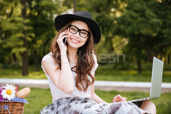 Cheerful woman alking on cell phone and using laptop outdoors Stock photo © deandrobot