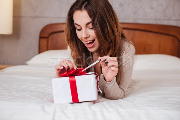 Stock photo: Woman opening present box while lying in bed at home