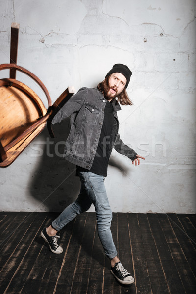 Bearded hipster man in hat throwing chair at camera Stock photo © deandrobot
