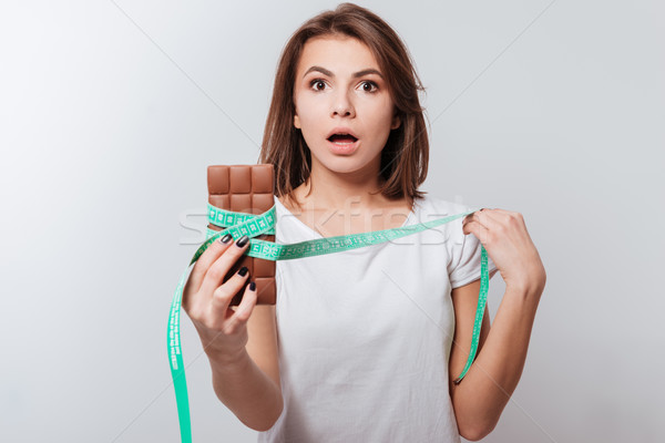 Confused young lady holding centimeter and chocolate Stock photo © deandrobot