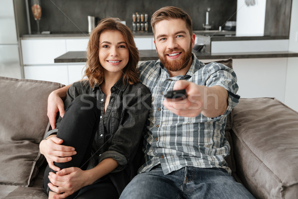 Cheerful loving couple sitting on sofa indoors and watching TV. Stock photo © deandrobot