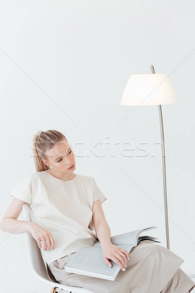 Concentrated blonde lady sitting indoors reading book. Stock photo © deandrobot